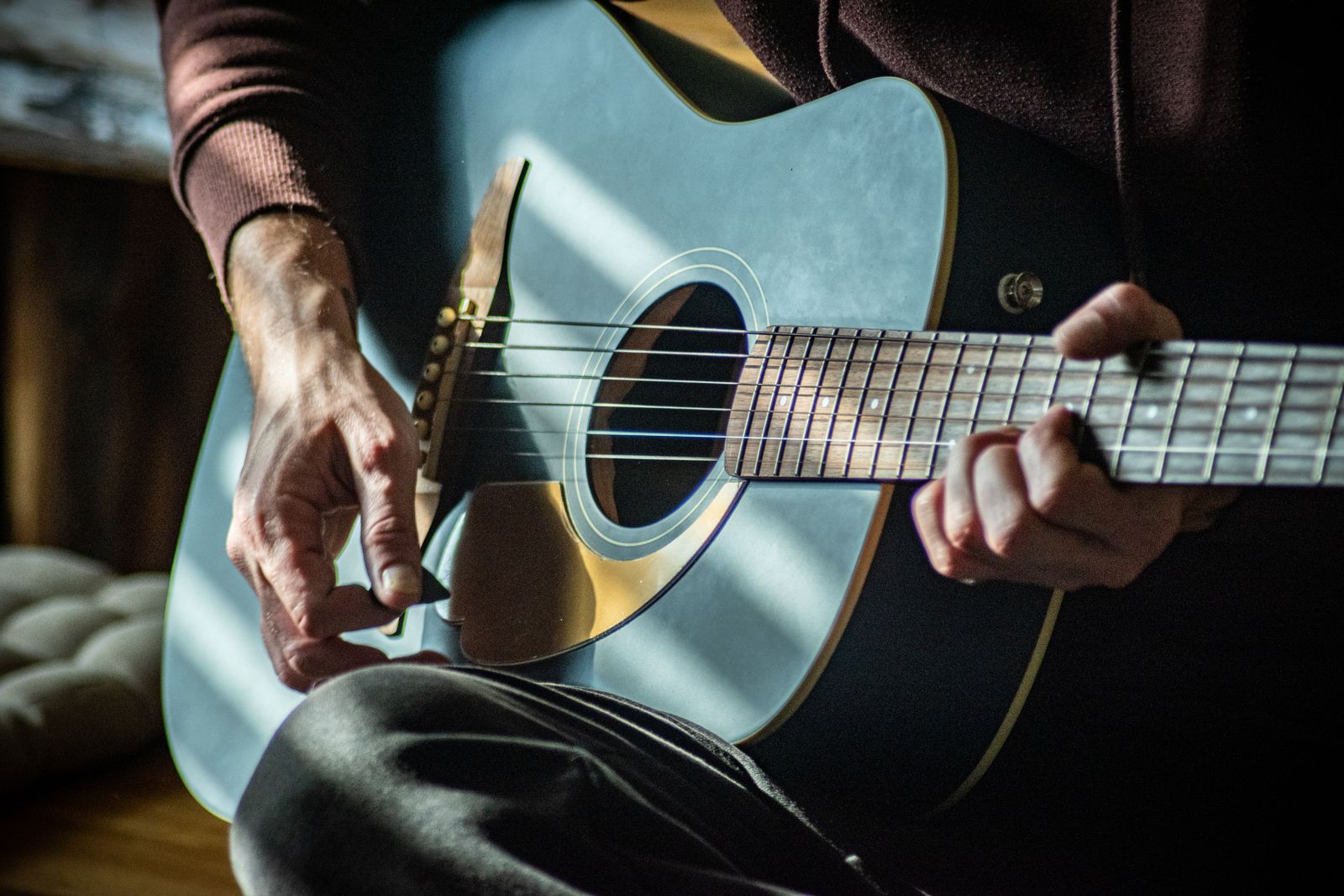 Musiker som spelar akustisk gitarr i ett soligt rum – bilden illustrerar den svenska vistraditionen