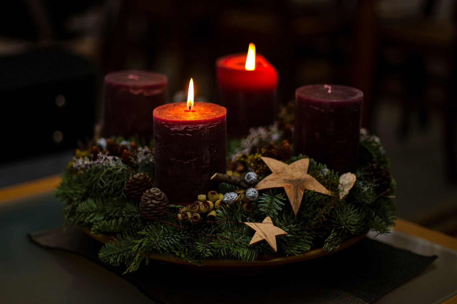 Tända ljus i en adventskrans med granris, kottar och stjärnor
