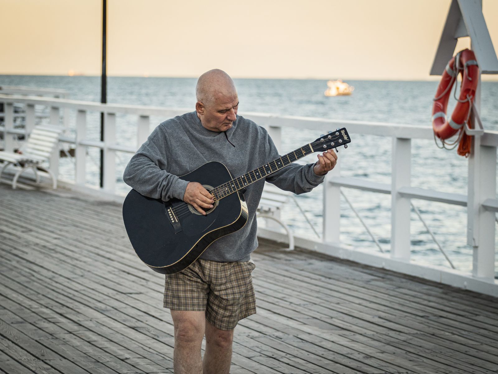 Man spelar akustisk gitarr på en brygga vid havet i solnedgången – illustration till artikel om Ted Gärdestad
