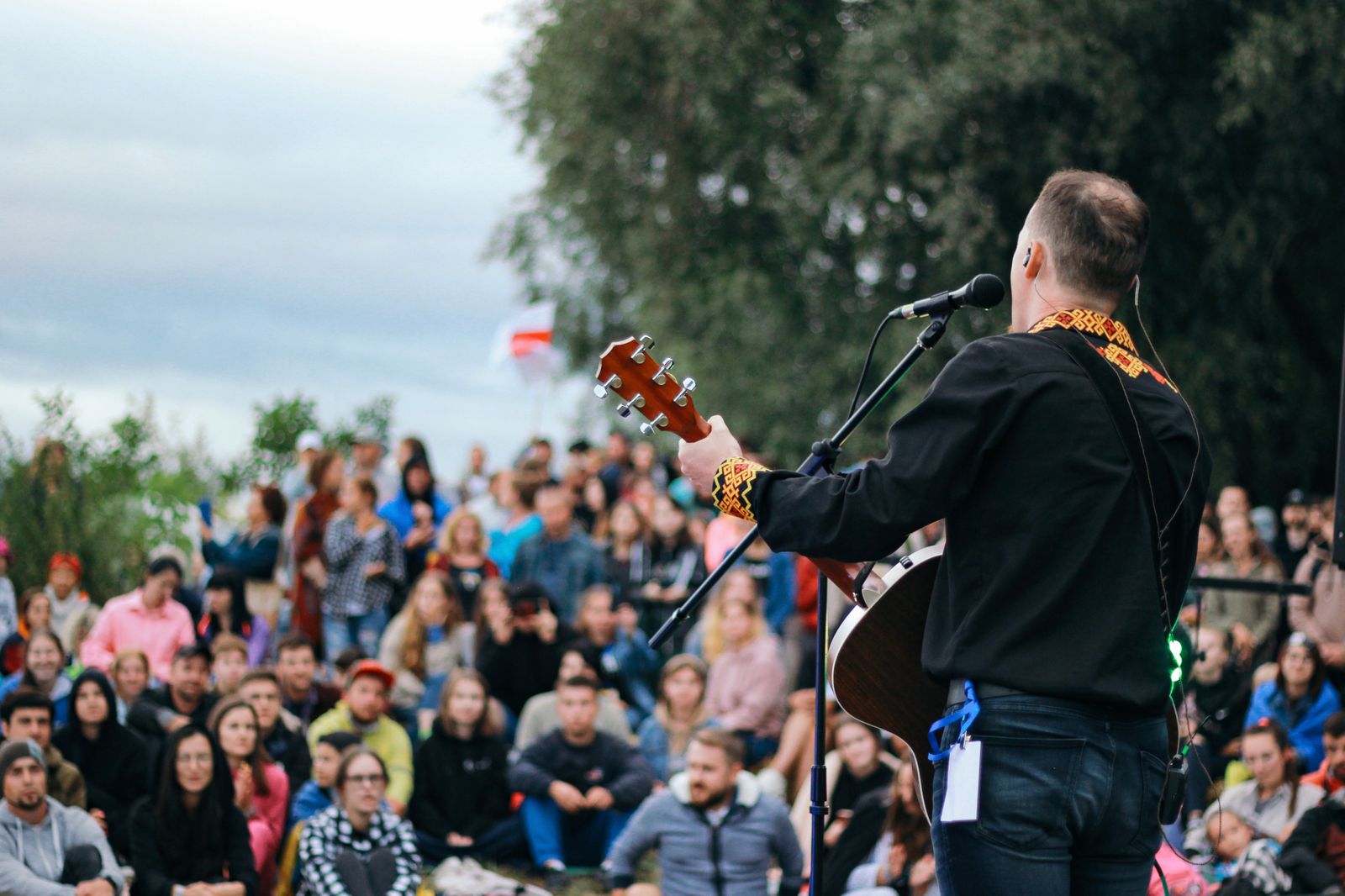 Artist med gitarr på utomhusscen framför publik en sommarkväll
