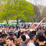 Festivalbesökare i sommarkläder framför en scen en solig dag
