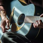 Musiker som spelar akustisk gitarr i ett soligt rum – bilden illustrerar den svenska vistraditionen
