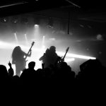 Siluetter av ett rockband på en scen med starkt motljus och publik framför