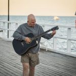 Man spelar akustisk gitarr på en brygga vid havet i solnedgången – illustration till artikel om Ted Gärdestad