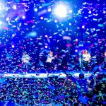 Jublande publik under färgglada scenljus med konfettiregn på en musikscen